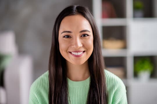 Professional headshot of a smiling woman in a mint green sweater against a blurred indoor background