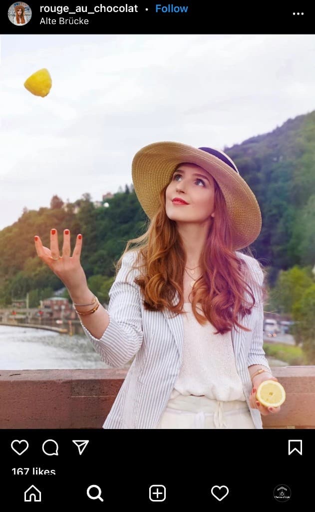 Woman in a straw hat tossing a lemon into the air on a bridge overlooking a river