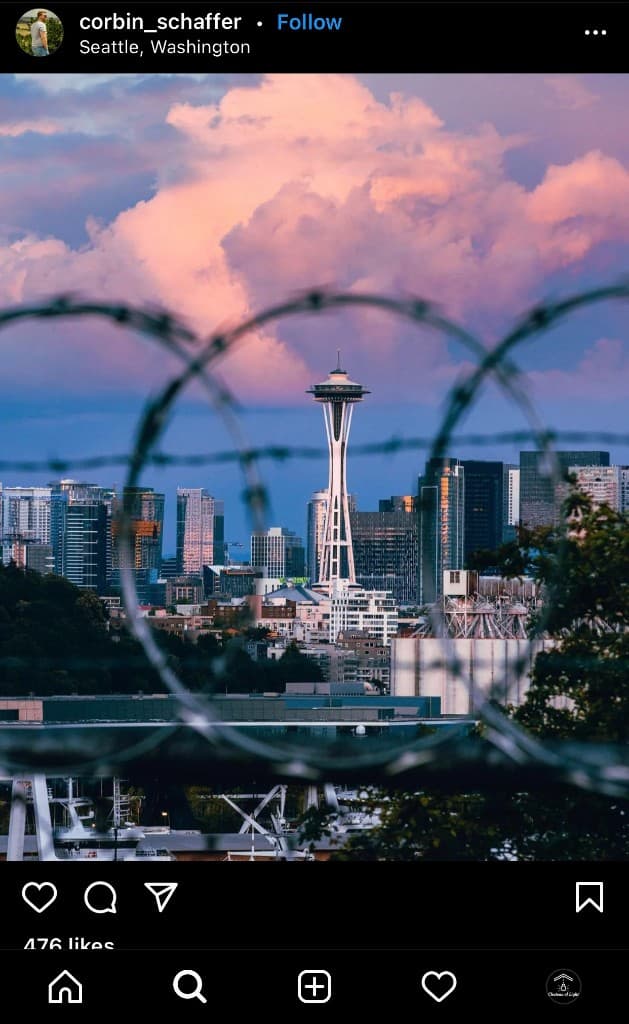 Seattle Space Needle at sunset, framed through blurred barbed wire loops under pink and orange clouds