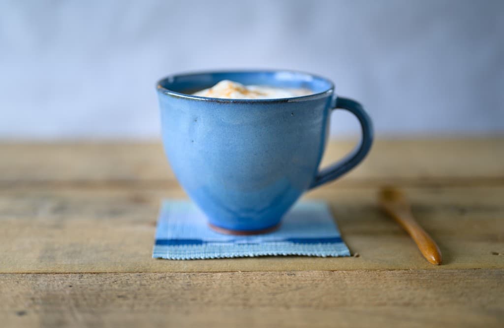 Blue ceramic mug with foamy latte and cinnamon on a wooden table.