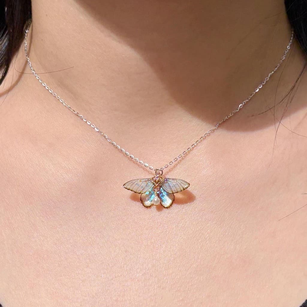 Silver chain necklace with an iridescent butterfly pendant and pearl accent worn on a person's neck