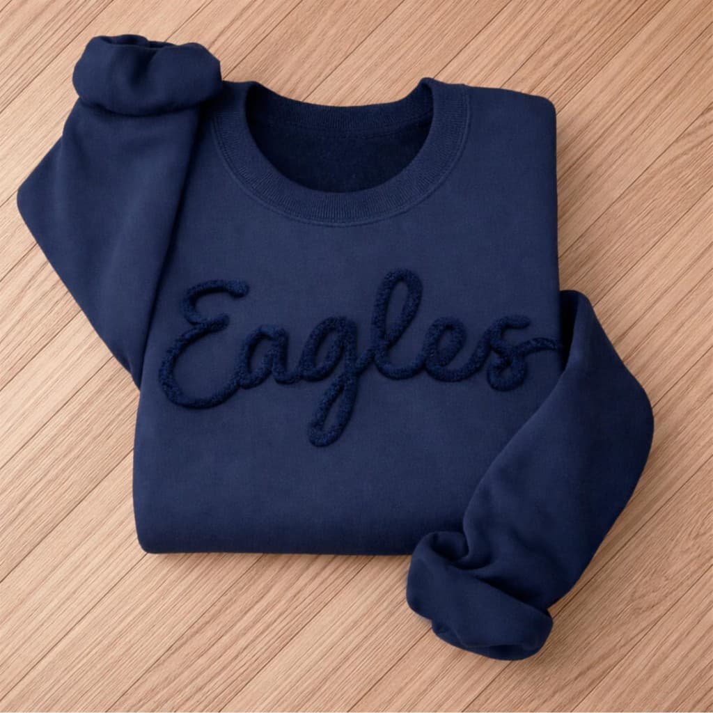 Navy blue sweatshirt folded on a wood surface with Eagles text in raised script lettering