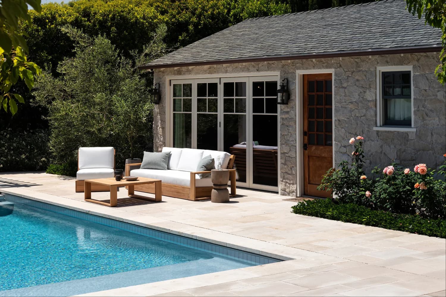 Outdoor patio with white lounge seating, stone wall, and poolside area